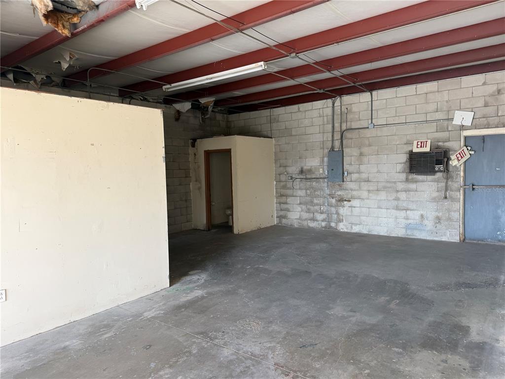An unfinished industrial space features exposed red ceiling beams, concrete block walls, and a restroom — 1706 N MAGNOLIA AVENUE UNIT 201, OCALA, FL