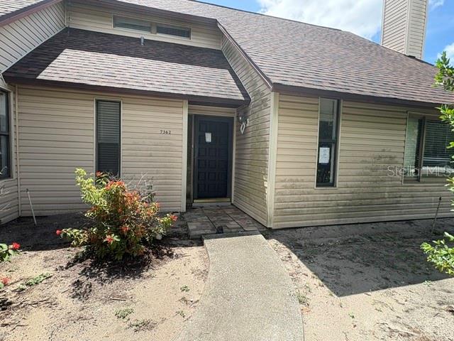 A beige-sided house features a dark front door, a concrete walkway, and a shingled roof — 7362 EDINBURGH WAY, WEEKI WACHEE, FL