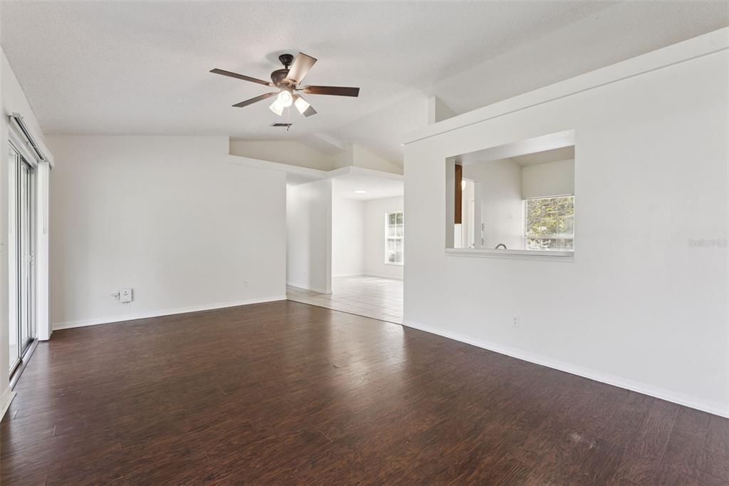 An empty living room features dark wood-look flooring, white walls, a ceiling fan, and a pass-through — 10803 SIENA DRIVE, CLERMONT, FL