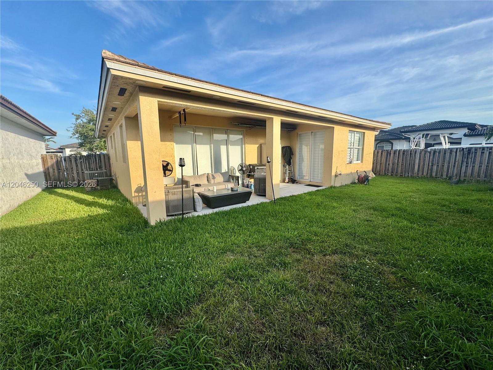 A tan house features a covered patio with outdoor furniture and a large grassy backyard — MIAMI, FL