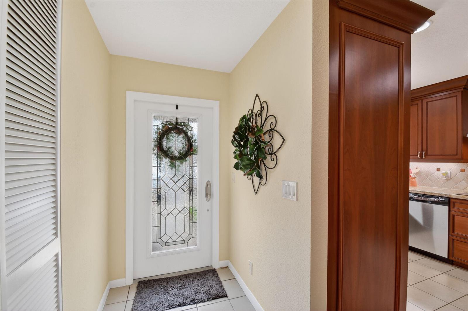 A foyer with a white front door, a wall wreath, and a view into the kitchen — 300 Cape Cod Circle, Lake Worth FL 33467, LAKE WORTH, FL