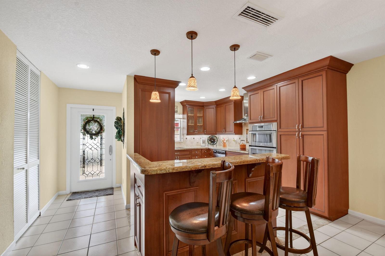 A kitchen features wood cabinets, granite countertops, a breakfast bar with stools, and tile flooring — 300 Cape Cod Circle, Lake Worth FL 33467, LAKE WORTH, FL
