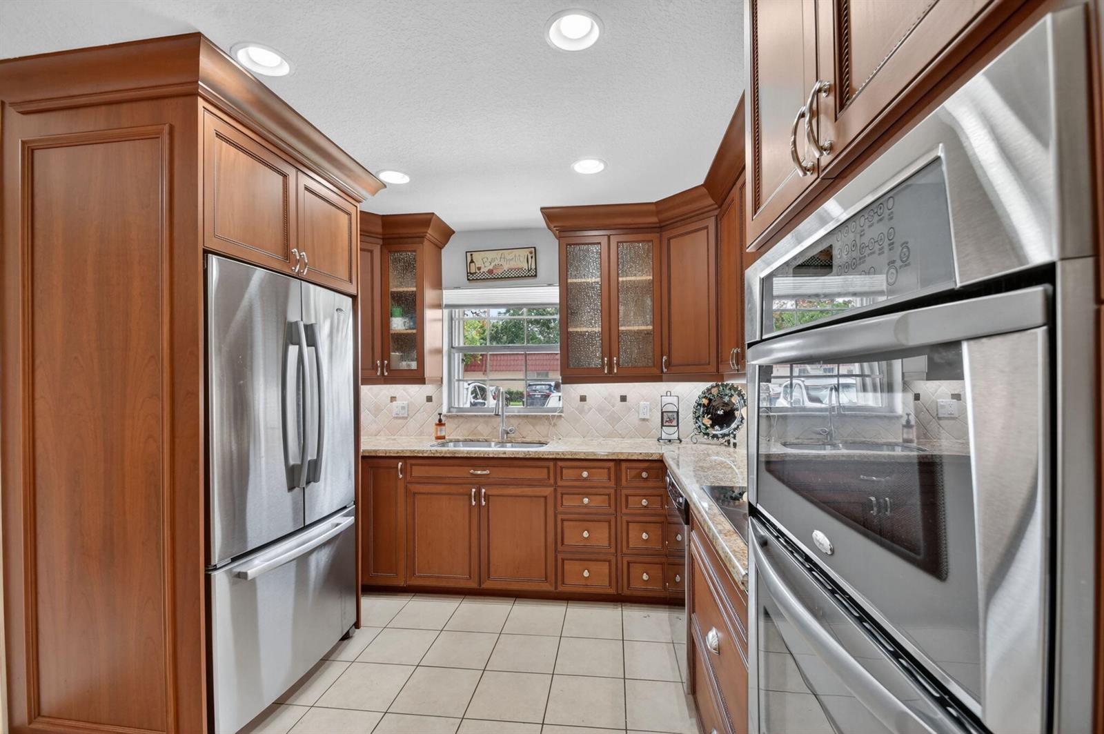 A kitchen features wood cabinets, stainless steel appliances, granite countertops, and light-colored tile flooring — 300 Cape Cod Circle, Lake Worth FL 33467, LAKE WORTH, FL