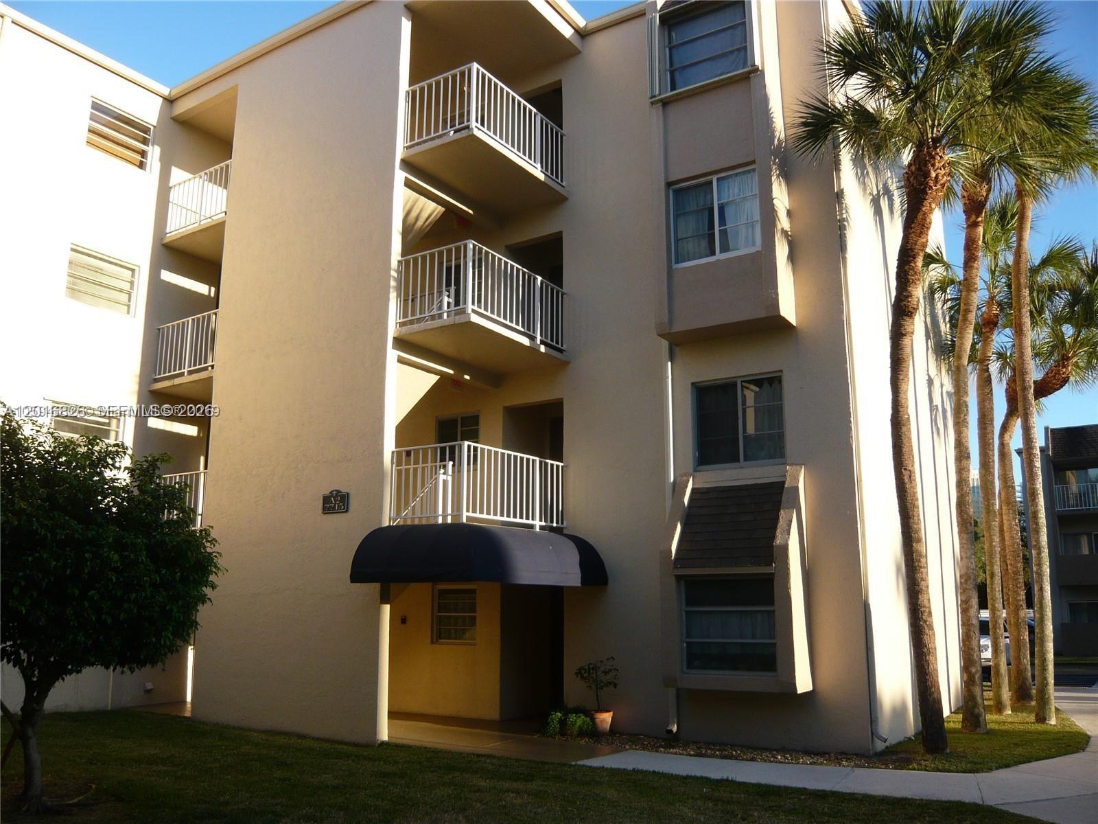 A multi-story apartment building features stacked balconies, a dark awning, and several palm trees — 7715 SW 86th St # 405, Miami FL 33143, MIAMI, FL