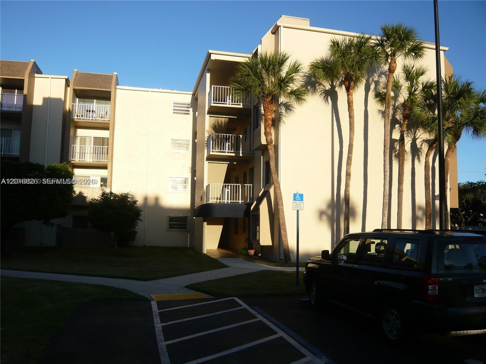A multi-story apartment building exterior features balconies, palm trees, and a parking lot — 7715 SW 86th St # 405, Miami FL 33143, MIAMI, FL