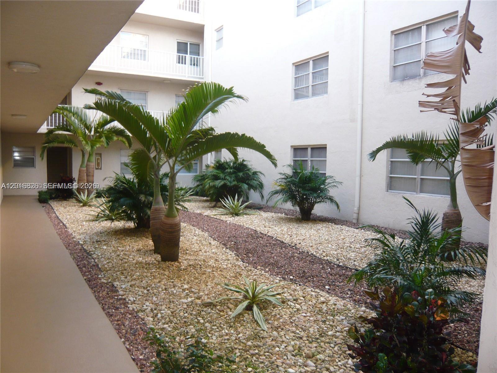 An outdoor courtyard features palm trees and decorative gravel landscaping between apartment building walls — 7715 SW 86th St # 405, Miami FL 33143, MIAMI, FL