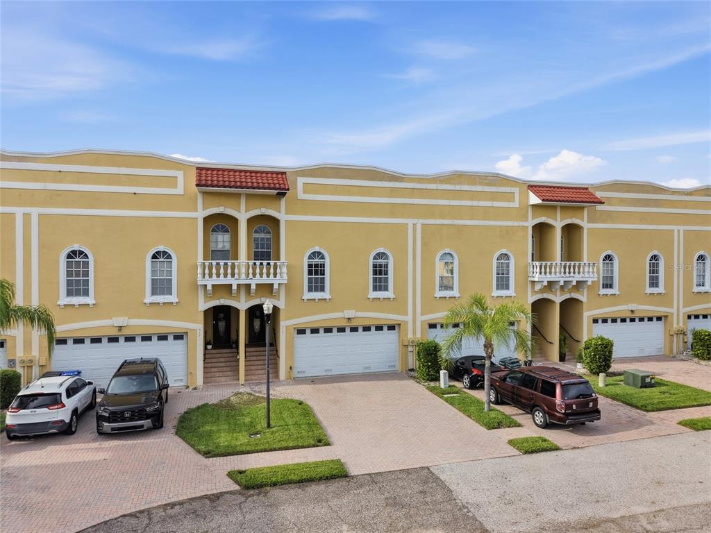 An exterior view of a multi-unit yellow townhouse complex with garages and paved driveways — 515 VILLA TREVISO COURT, APOLLO BEACH, FL