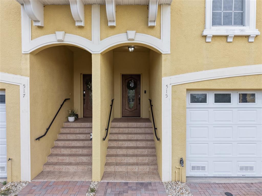 The exterior of a yellow townhouse features two arched entryways with stairs and garage doors — 515 VILLA TREVISO COURT, APOLLO BEACH, FL