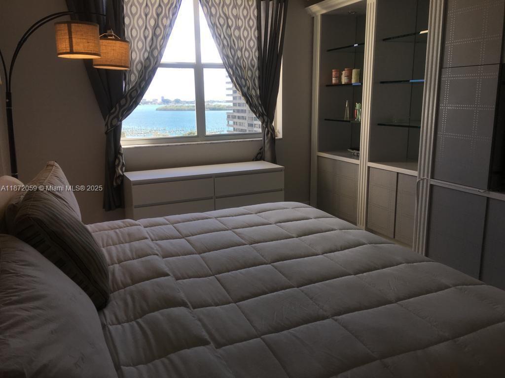A bedroom features a bed, built-in shelving, a dresser, and a window with water views — 11111 Biscayne Blvd # 4D, Miami FL 33181, MIAMI, FL