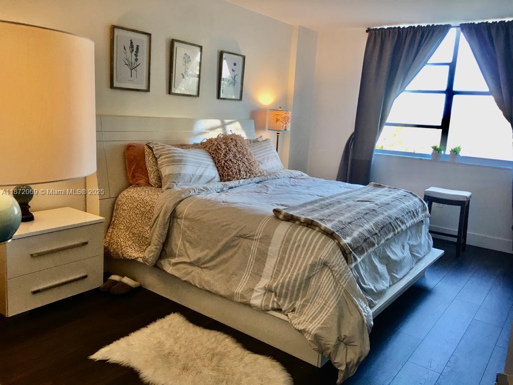 A bedroom features a bed with striped bedding, a white headboard, and dark wood flooring — 11111 Biscayne Blvd # 4D, Miami FL 33181, MIAMI, FL