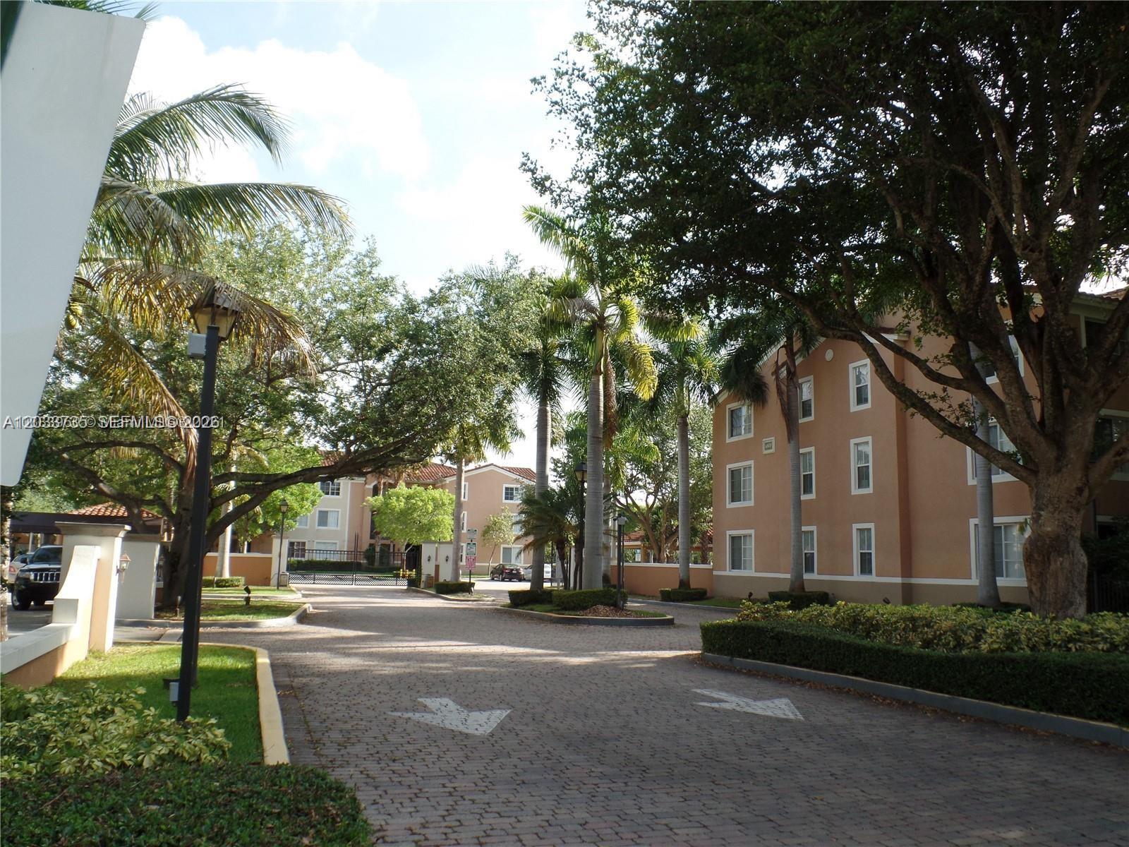 A paved driveway leads toward multi-story apartment buildings surrounded by palm trees and landscaping — 6801 SW 44th St # 203, Miami FL 33155, MIAMI, FL