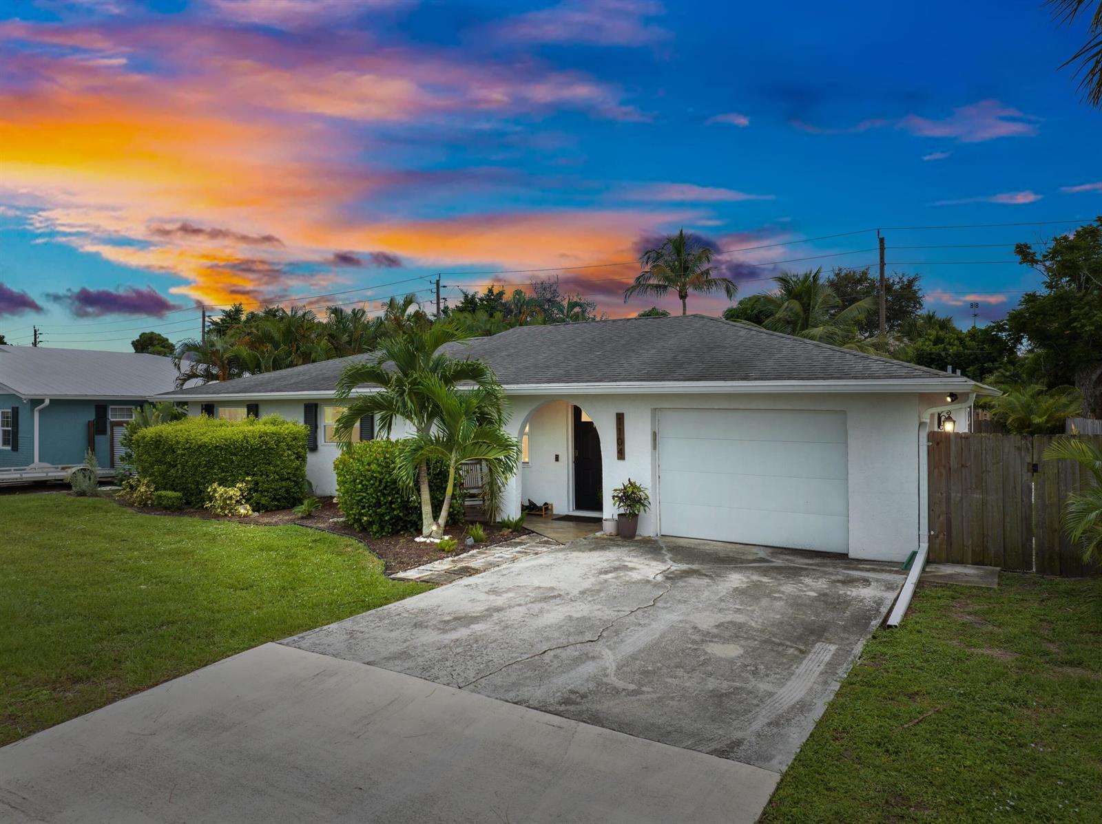 A white single-story house with a garage and palm trees under a colorful sunset sky — 1104 NW 12th Terrace, Stuart FL 34994, STUART, FL