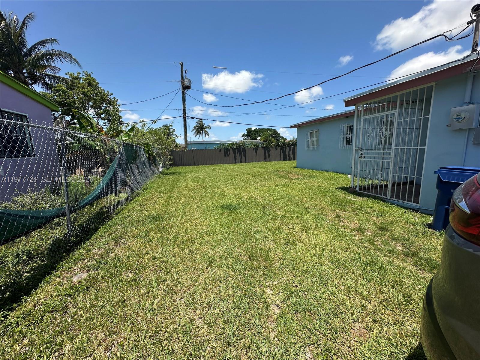 A grassy backyard sits between a light blue house and a chain-link fence — 10761 SW 221st St, Miami FL 33170, MIAMI, FL