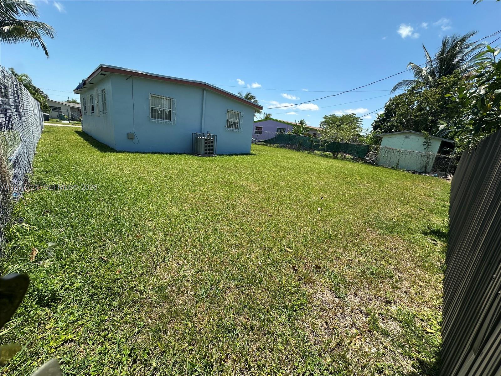 A light blue house sits on a grassy lot enclosed by chain-link and wooden fences — 10761 SW 221st St, Miami FL 33170, MIAMI, FL