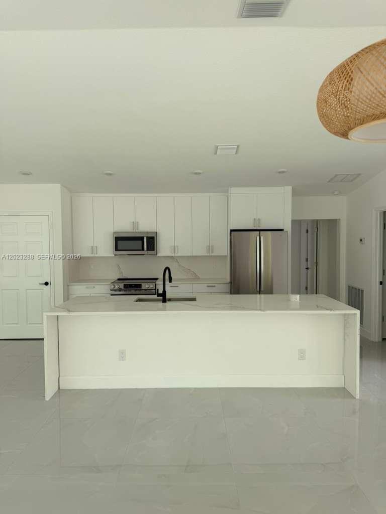 A modern kitchen features white cabinetry, a large waterfall island, and stainless steel appliances — 8636 100th Ct, Vero Beach FL 32967, VERO BEACH, FL