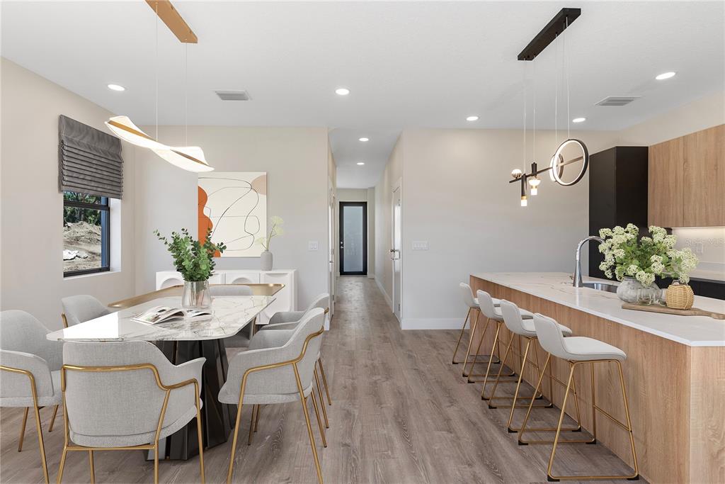 A modern dining area and kitchen feature light wood cabinetry, marble countertops, and gray upholstered chairs — 8456 MODANO PLACE, TAMPA, FL