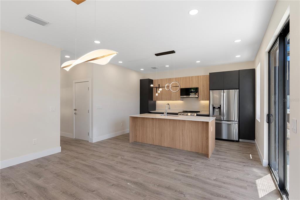 A modern kitchen features light wood cabinets, a central island, stainless steel appliances, and wood-look flooring — 8456 MODANO PLACE, TAMPA, FL