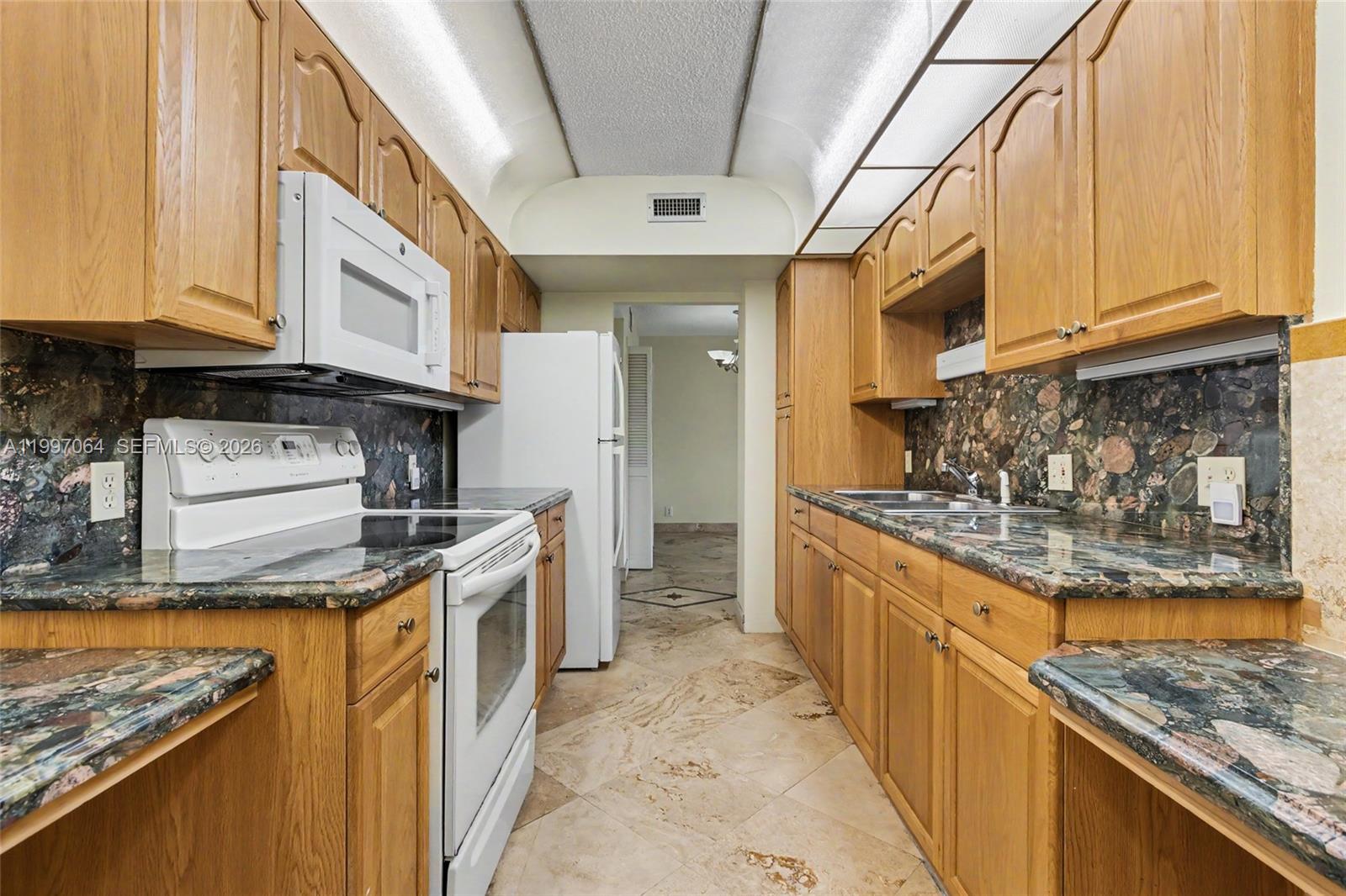 A galley kitchen features oak cabinets, dark granite countertops, and white appliances — 4200 Hillcrest Dr # 408, Hollywood FL 33021, HOLLYWOOD, FL
