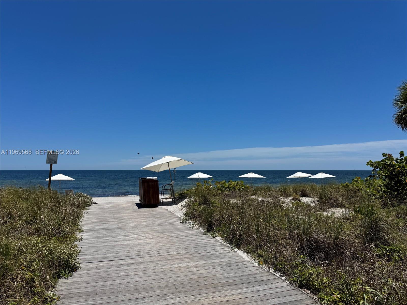 A wooden boardwalk leads to a beach with several white umbrellas under a clear sky — 350 Ocean Dr # 406N, Key Biscayne FL 33149, KEY BISCAYNE, FL