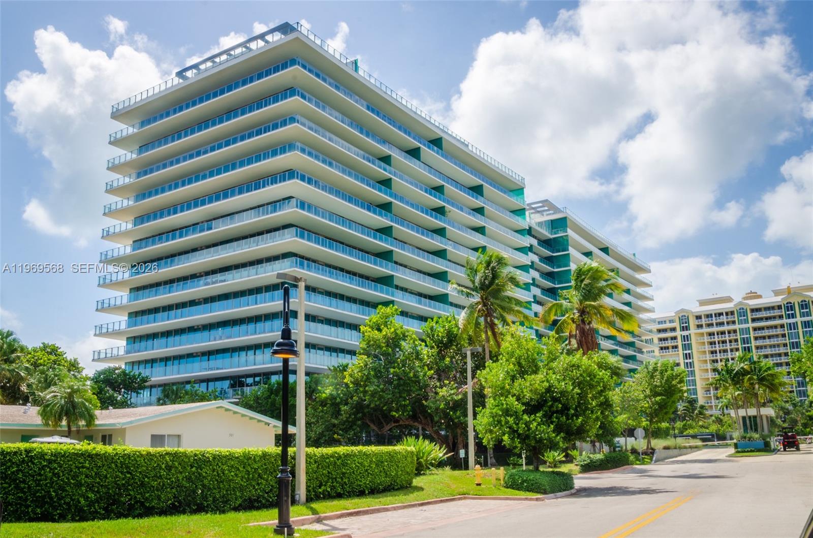 A modern multi-story residential building with glass balconies stands behind lush green landscaping — 350 Ocean Dr # 406N, Key Biscayne FL 33149, KEY BISCAYNE, FL