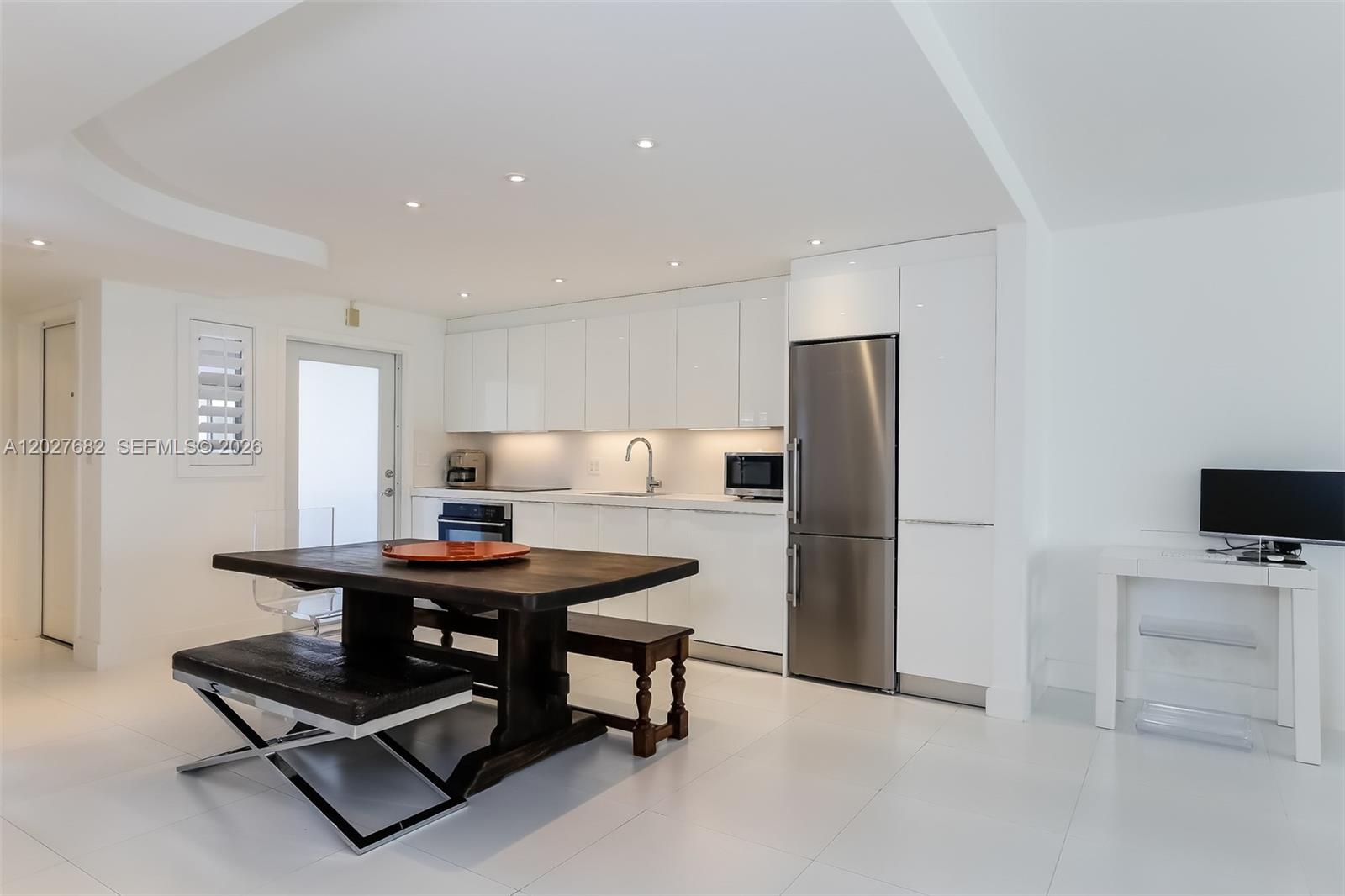 A modern kitchen features white cabinetry, stainless steel appliances, and a dark wood dining set — 200 Galen Dr # 104, Key Biscayne FL 33149, KEY BISCAYNE, FL