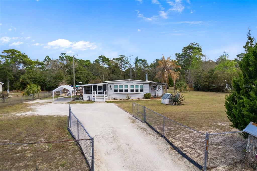 A light-colored single-story house with a screened porch sits behind a fenced gravel driveway — 2901 S PINE RIDGE AVENUE, HOMOSASSA, FL
