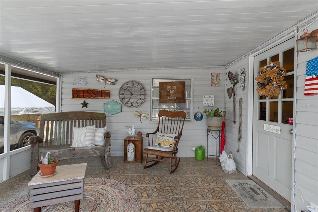 A covered porch features a wooden bench, a rocking chair, wall decor, and tiled flooring — 2901 S PINE RIDGE AVENUE, HOMOSASSA, FL