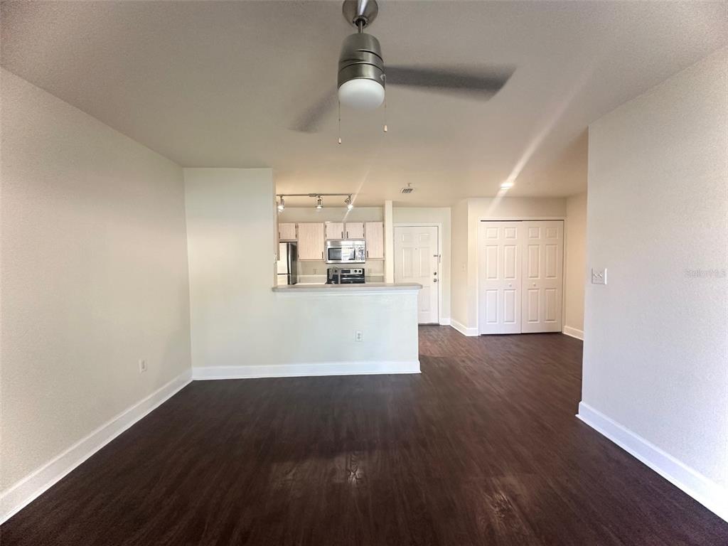 An open-concept living area features dark wood-look flooring, a ceiling fan, and a kitchen pass-through — 5467 VINELAND ROAD UNIT 6114, ORLANDO, FL