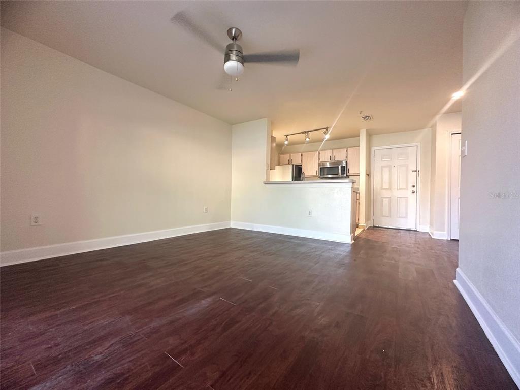 An open-concept living area with dark wood-look flooring leads to a kitchen with light cabinetry — 5467 VINELAND ROAD UNIT 6114, ORLANDO, FL