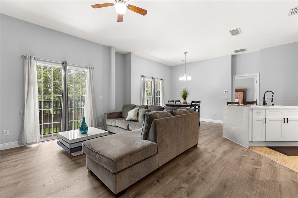 A living room with light wood floors, a gray sectional sofa, and a sliding glass door — 2026 ESTANCIA CIRCLE UNIT A, KISSIMMEE, FL