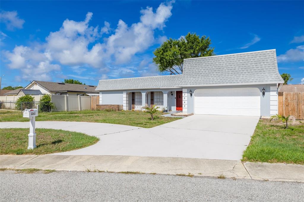 A single-story house with a gray roof, white garage door, and a red front door — 3543 ROCKAWAY DRIVE, HOLIDAY, FL