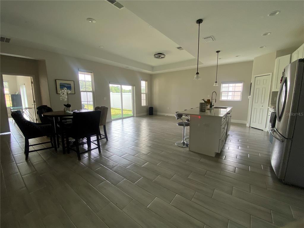 An open-concept kitchen and dining area features light-colored tile flooring and a central island — 4995 MERCER STREET, ORLANDO, FL