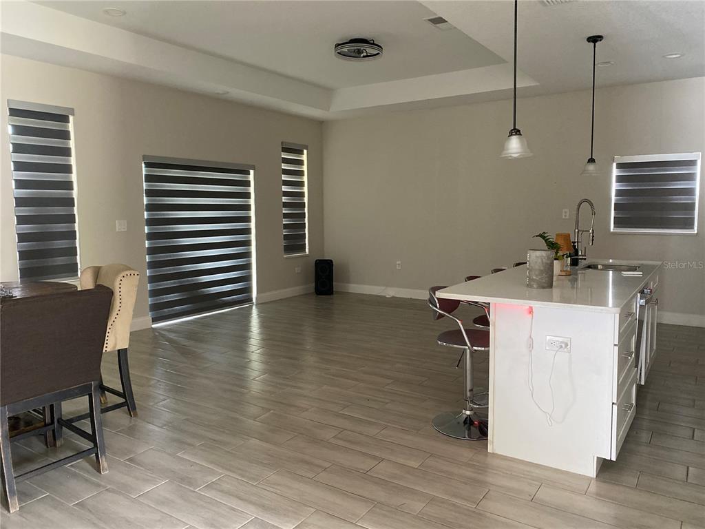 An open-concept kitchen and living area features light wood-look tile floors and a white island — 4995 MERCER STREET, ORLANDO, FL