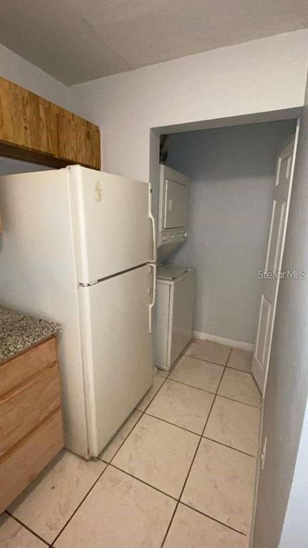 A white refrigerator stands in a kitchen next to a laundry closet with stacked appliances — 5214 VIA HACIENDA CIRCLE UNIT A306, ORLANDO, FL