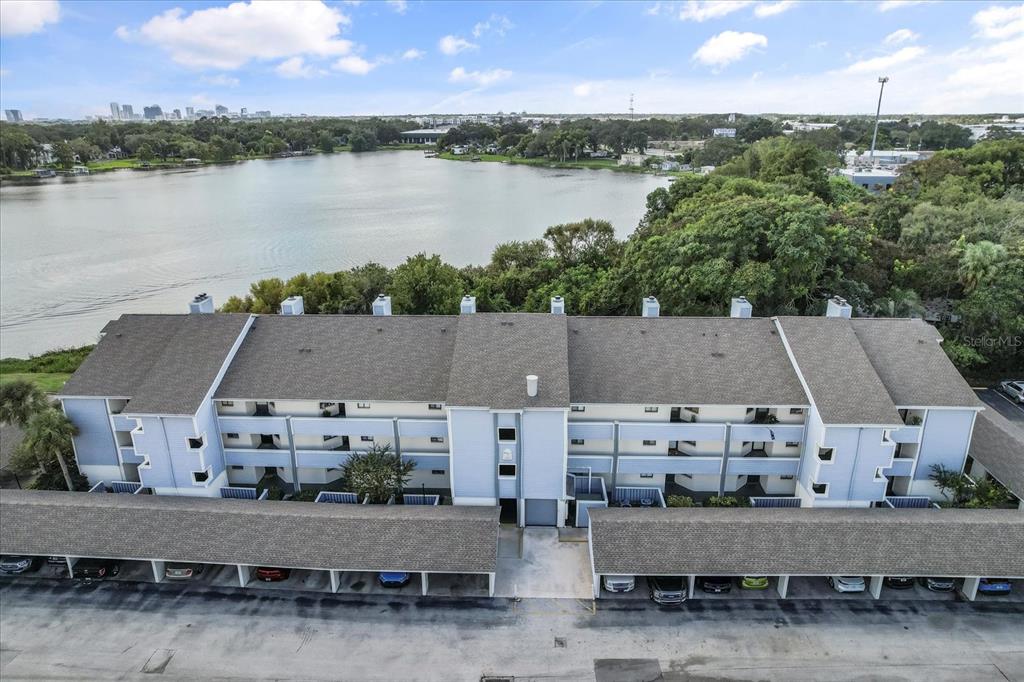An aerial view shows a multi-story apartment building with covered parking in front of a lake — 4101 FAIRVIEW VISTA POINT UNIT 130, ORLANDO, FL