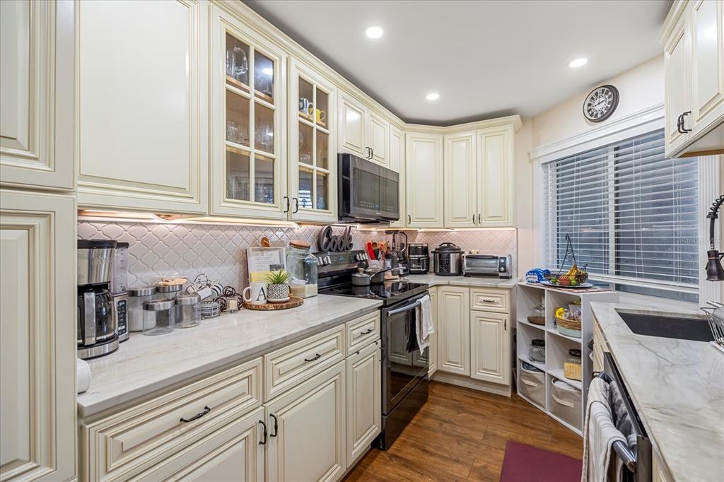 A kitchen features cream-colored cabinets, marble-look countertops, a black stove, and a tile backsplash — 4101 FAIRVIEW VISTA POINT UNIT 130, ORLANDO, FL