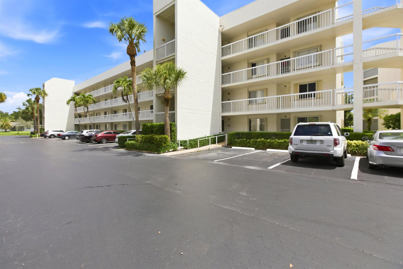 A multi-story apartment building with a parking lot and palm trees in front — 3146 Via Poinciana # 407, FL 33467, FL