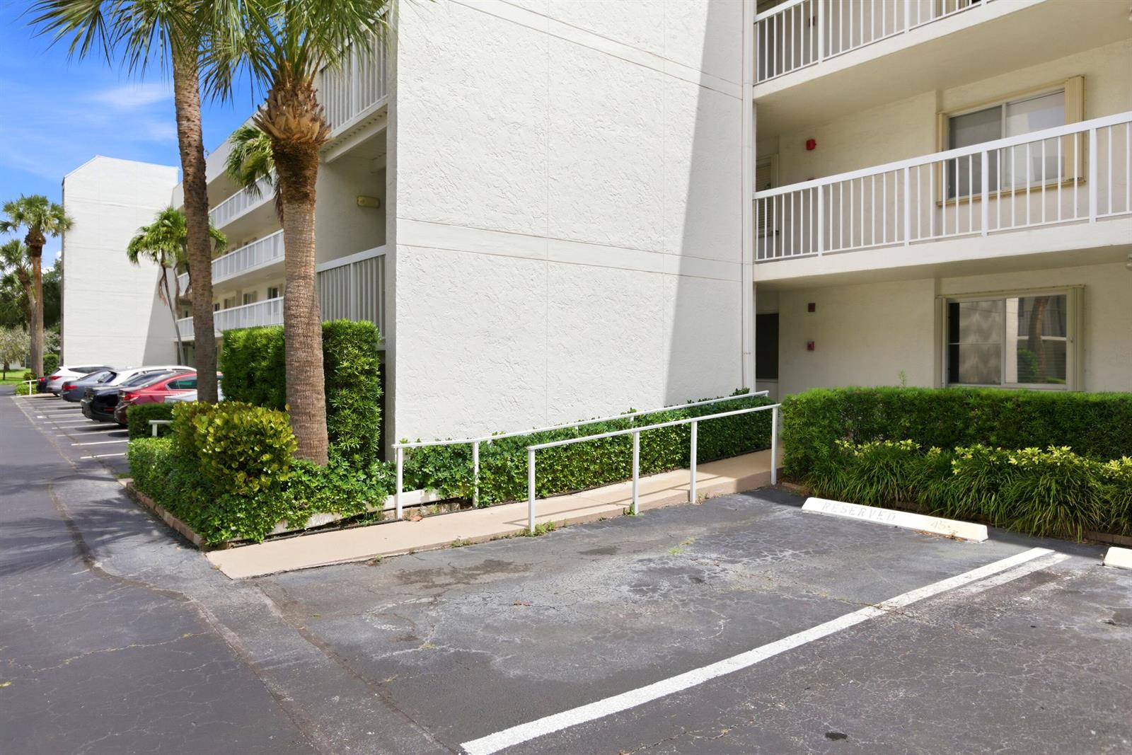 An exterior view shows a multi-story apartment building with a wheelchair ramp and parking spaces — 3146 Via Poinciana # 407, FL 33467, FL