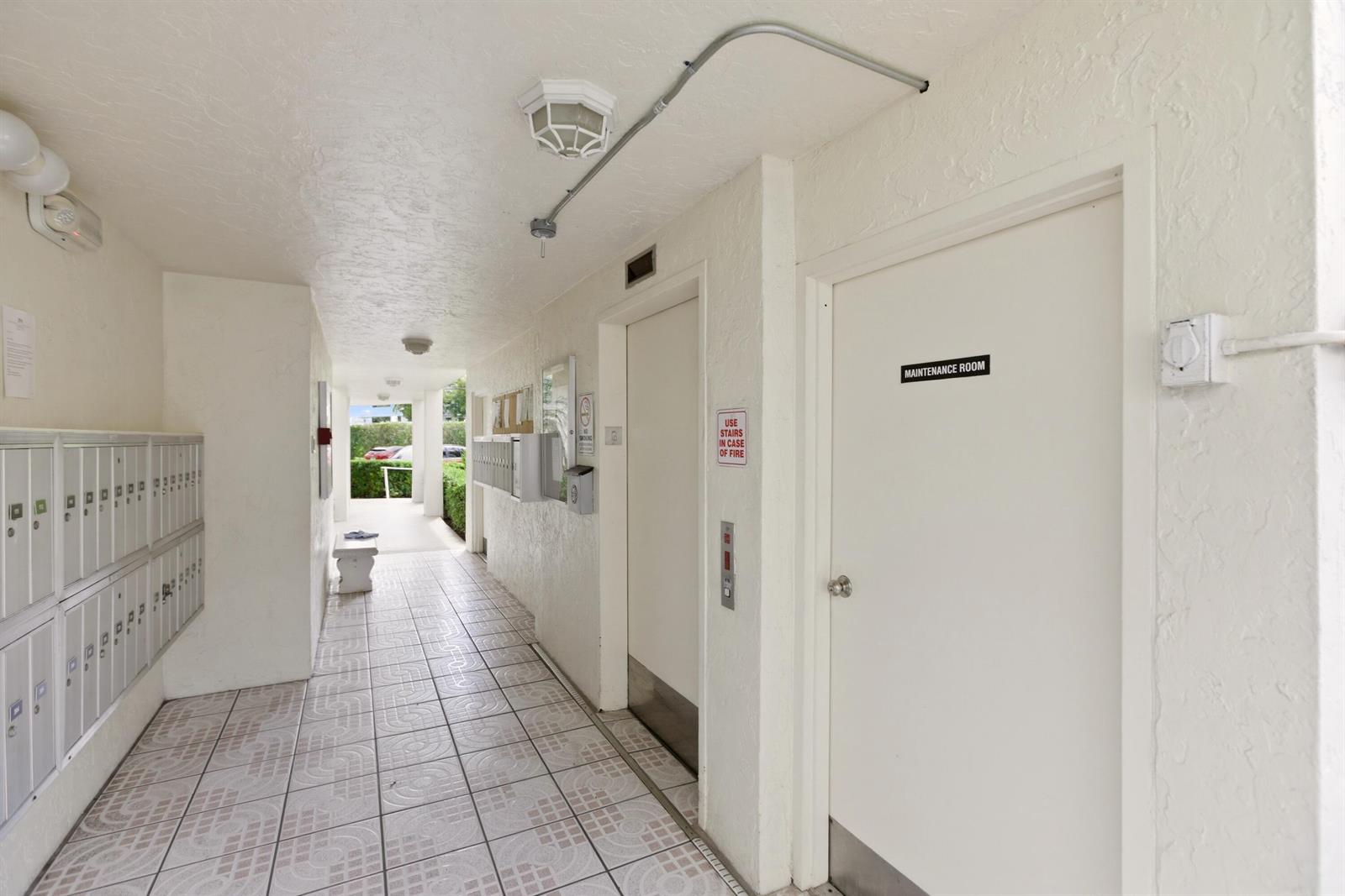 A hallway features mailboxes, an elevator, a maintenance room door, and tiled flooring — 3146 Via Poinciana # 407, FL 33467, FL