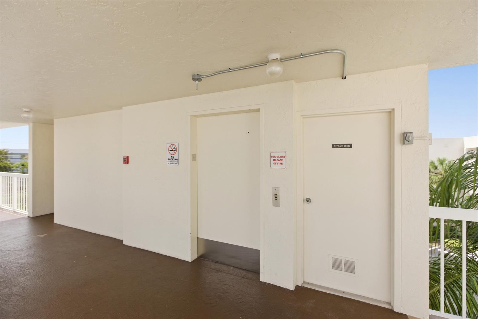 An outdoor hallway features an elevator, a storage room door, and a no-smoking sign — 3146 Via Poinciana # 407, FL 33467, FL