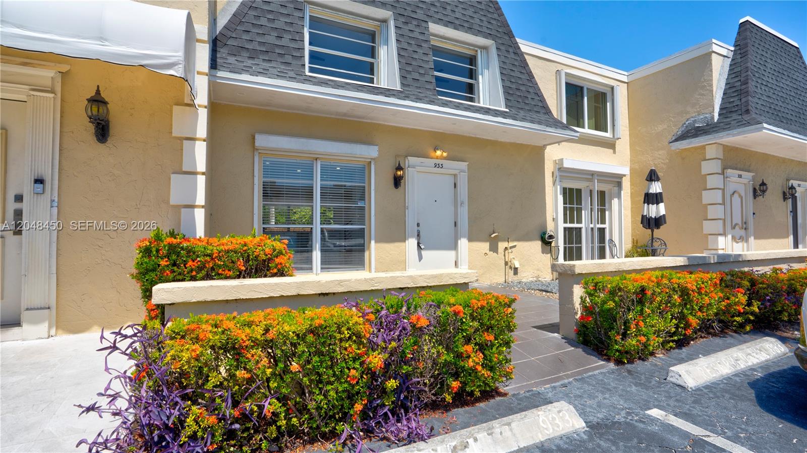 The exterior of a tan townhouse features a mansard roof, a front door, and landscaping — 933 NE 24th Ave # 169, Hallandale Beach FL 33009, HALLANDALE BEACH, FL