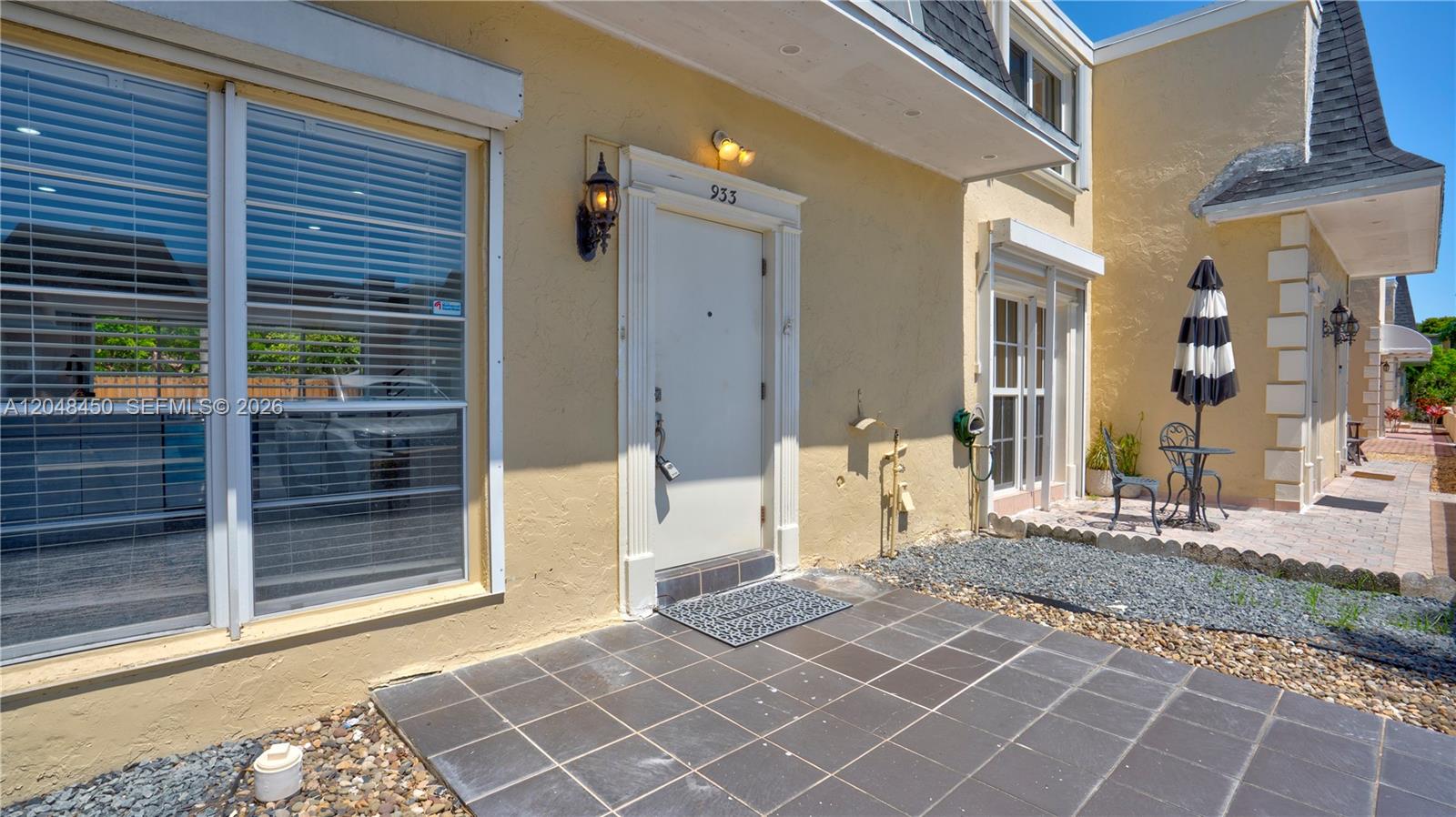 The exterior of a yellow building features a white front door, tiled patio, and windows — 933 NE 24th Ave # 169, Hallandale Beach FL 33009, HALLANDALE BEACH, FL