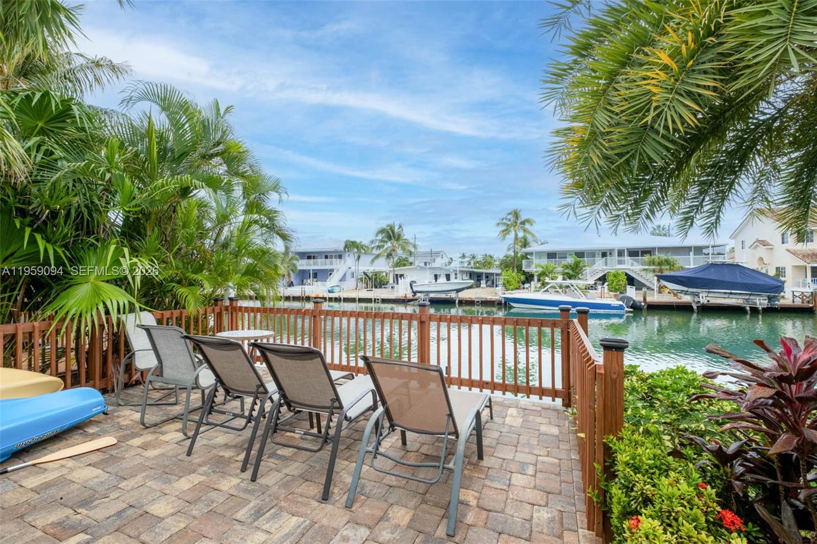 A paved patio with lounge chairs overlooks a canal with docked boats and palm trees — 410 10th St, Key Colony FL 33051, KEY COLONY, FL