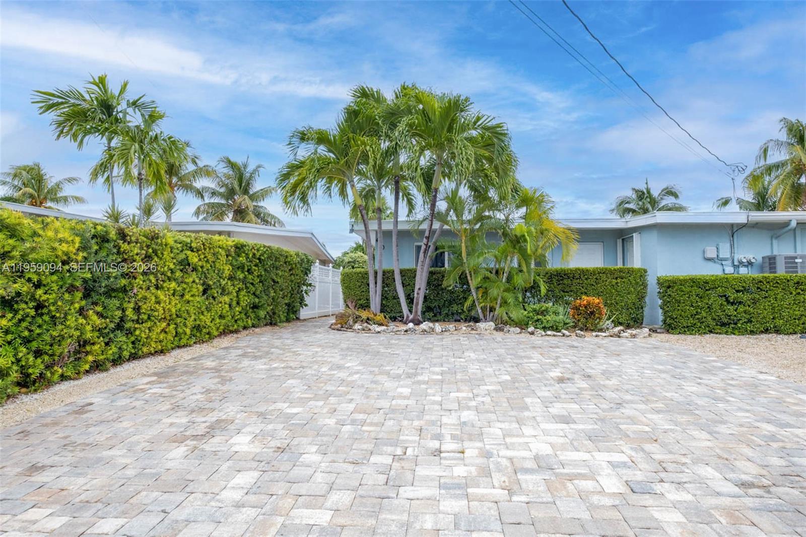 A paved driveway leads to a light blue house surrounded by tall green hedges — 410 10th St, Key Colony FL 33051, KEY COLONY, FL