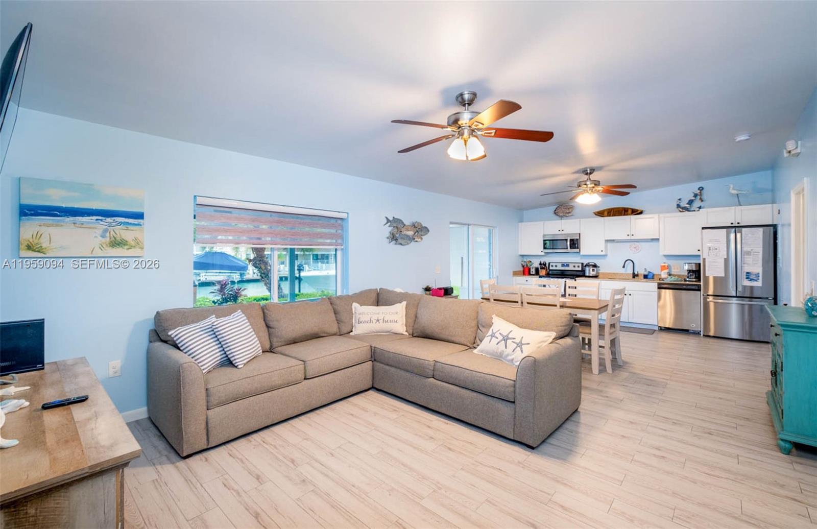 An open-concept living and dining area features a sectional sofa, light wood floors, and kitchen — 410 10th St, Key Colony FL 33051, KEY COLONY, FL
