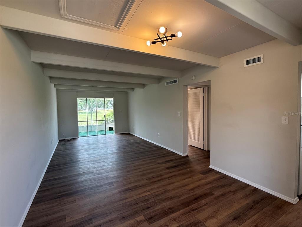 An empty living room features wood-look flooring, exposed ceiling beams, and a sliding glass door — 3421 CLUB CIRCLE, LAKESHORE, FL