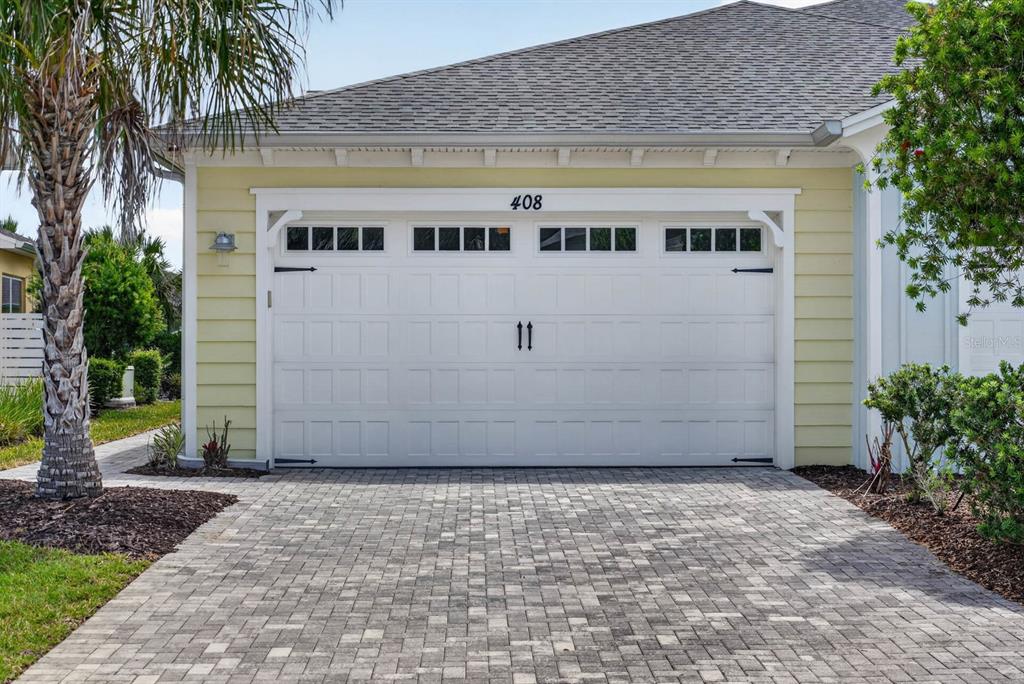 A pale yellow house features a white two-car garage door with windows and a paver driveway — 408 LOST SHAKER WAY, DAYTONA BEACH, FL