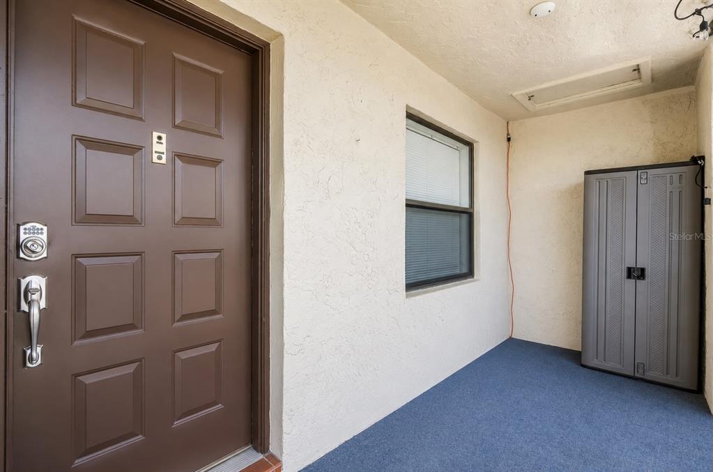 A brown front door with a keypad lock opens onto a covered porch with blue carpet — 7178 GOLF COLONY COURT UNIT 202, LAKE WORTH, FL