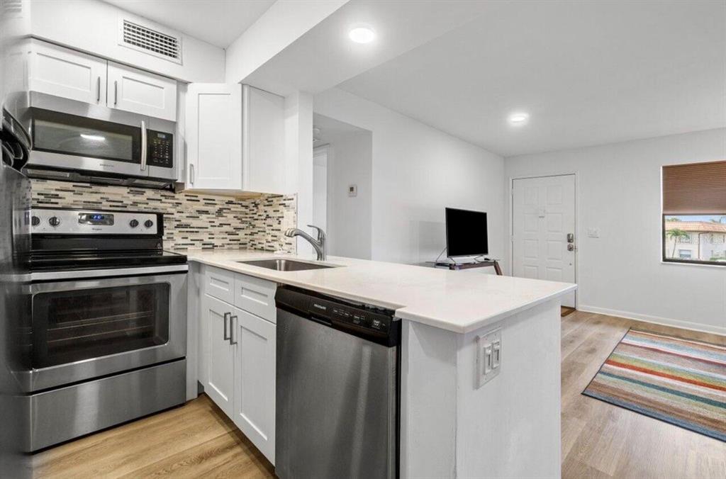 A kitchen with white cabinets, stainless steel appliances, and a breakfast bar overlooking a living area — 7178 GOLF COLONY COURT UNIT 202, LAKE WORTH, FL