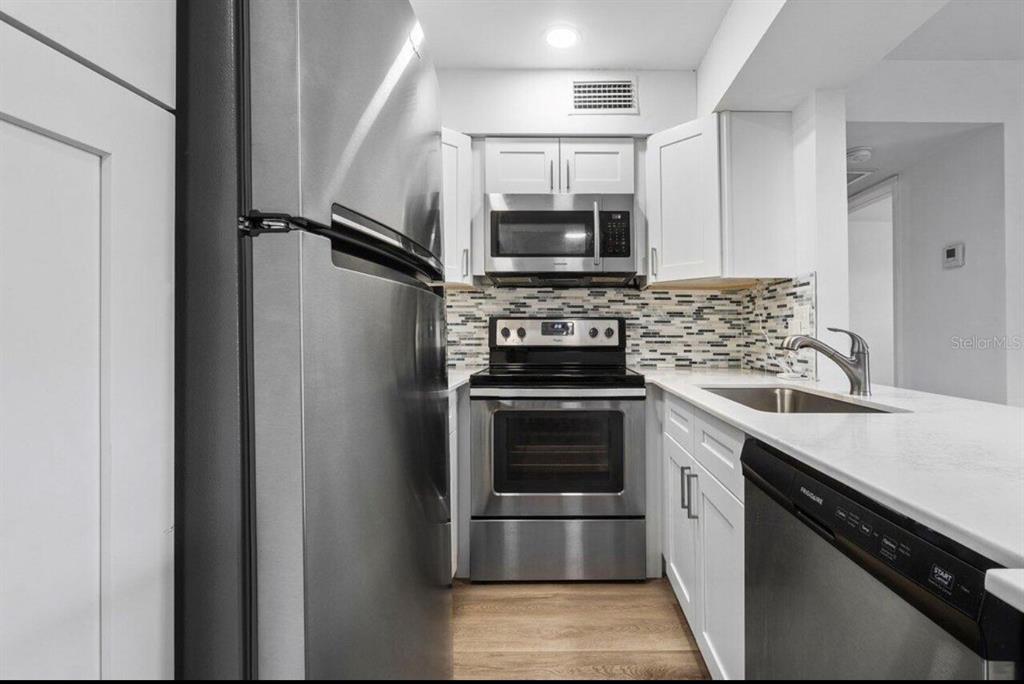 A galley kitchen features white cabinets, stainless steel appliances, and a mosaic tile backsplash — 7178 GOLF COLONY COURT UNIT 202, LAKE WORTH, FL